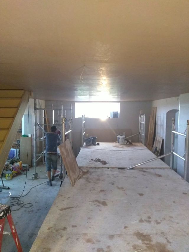 Plastering under way in a large open room, with boards laid across the floor